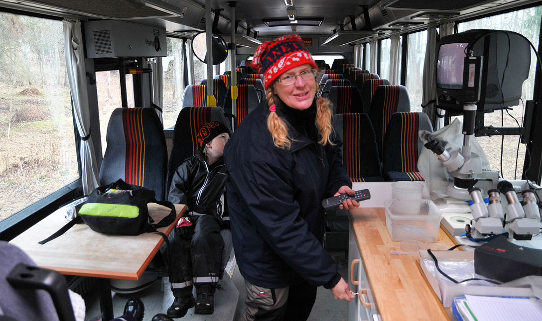 Anette Aspegren-Güldorff inne i bussen vid tv och mikroskåp. En pojke sitter i bussen.