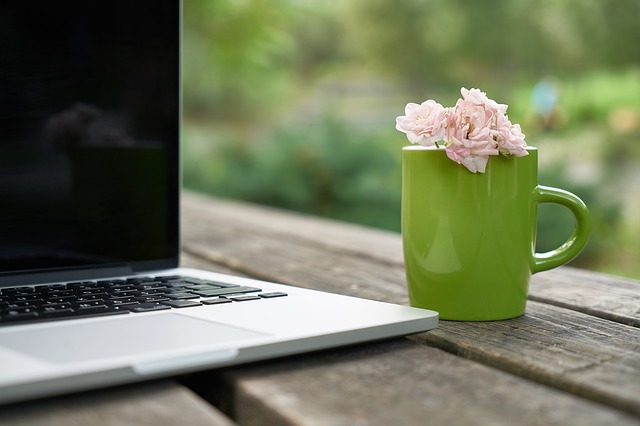 Laptop. Rosa blommor i grön kaffekopp på ett träbord