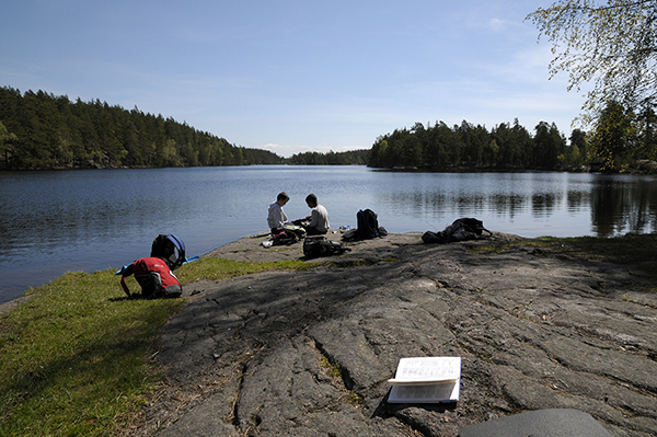 Två barn sitter på en badklippa. En lärobok i förgrunden.